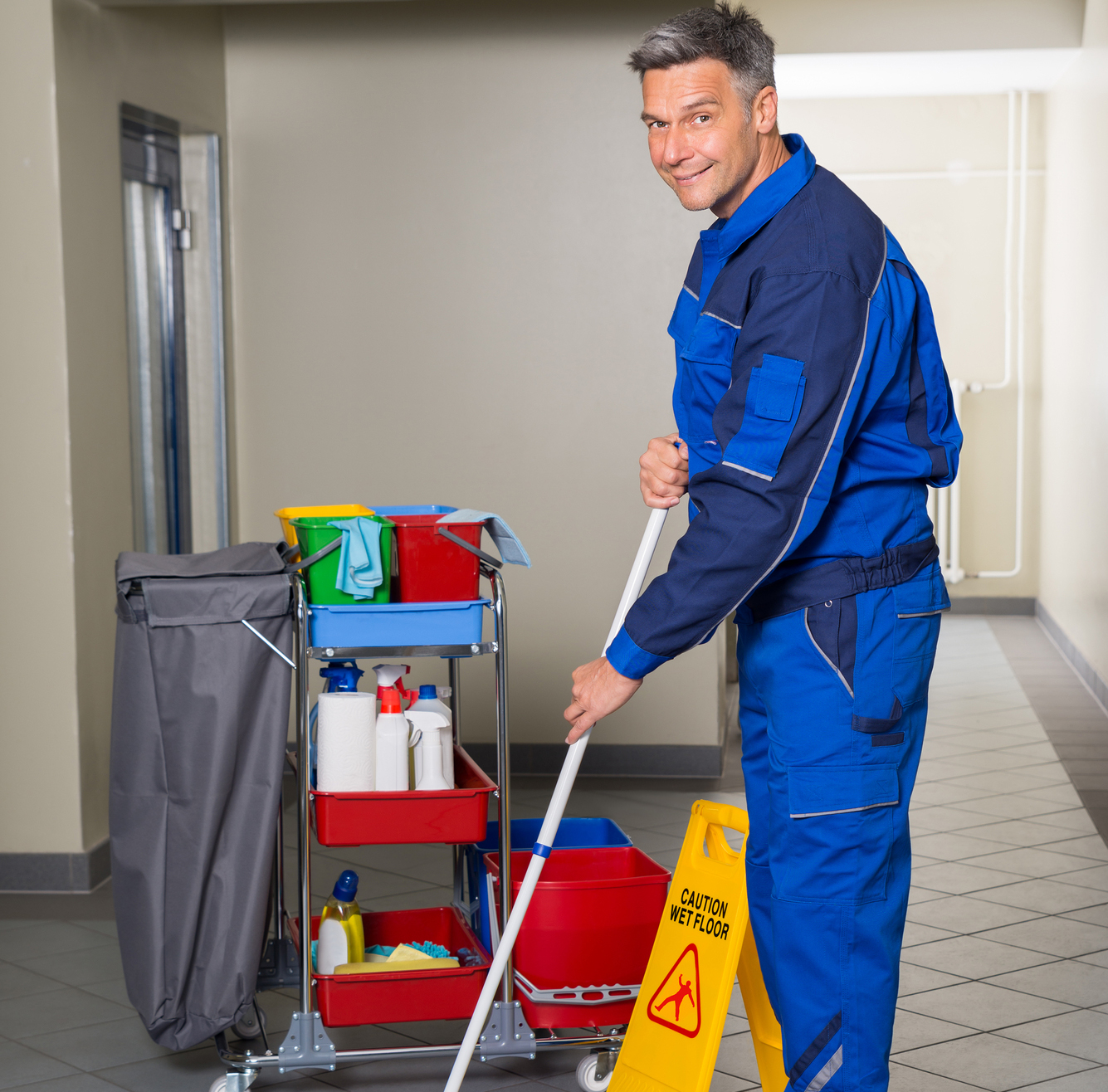 Full length of mature male worker with broom cleaning corridor